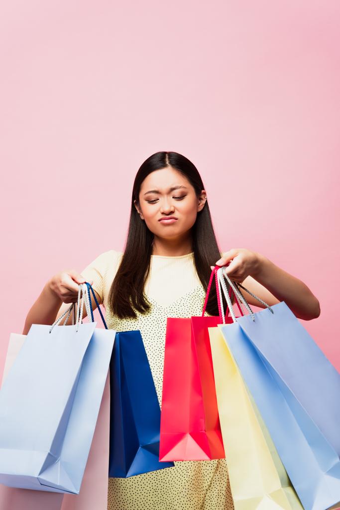 descontente asiático menina olhando para compras sacos isolado no rosa
  - Foto, Imagem