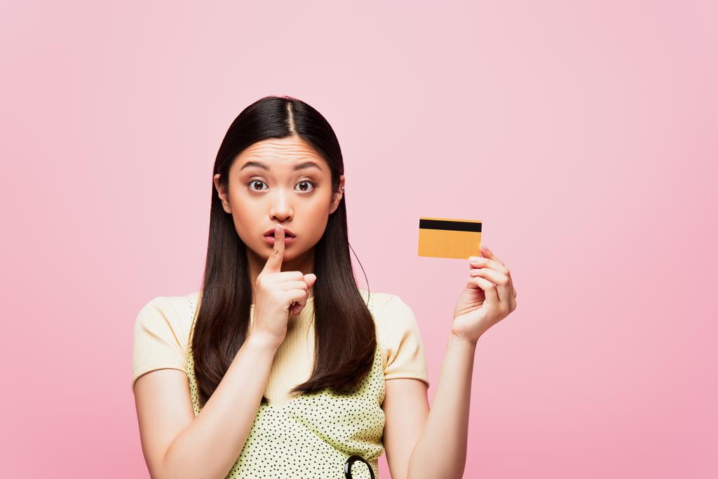 若いアジアの女性がクレジットカードを持っていてピンクに孤立した  - 写真・画像