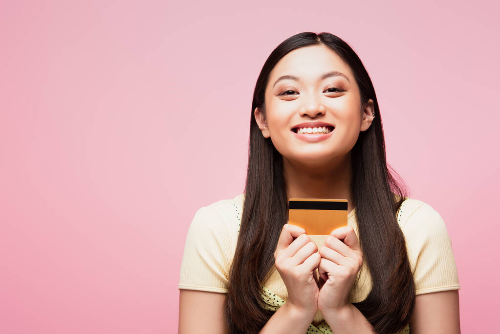 陽気で若いアジア系女性がピンクで孤立したクレジットカードを持っていて  - 写真・画像