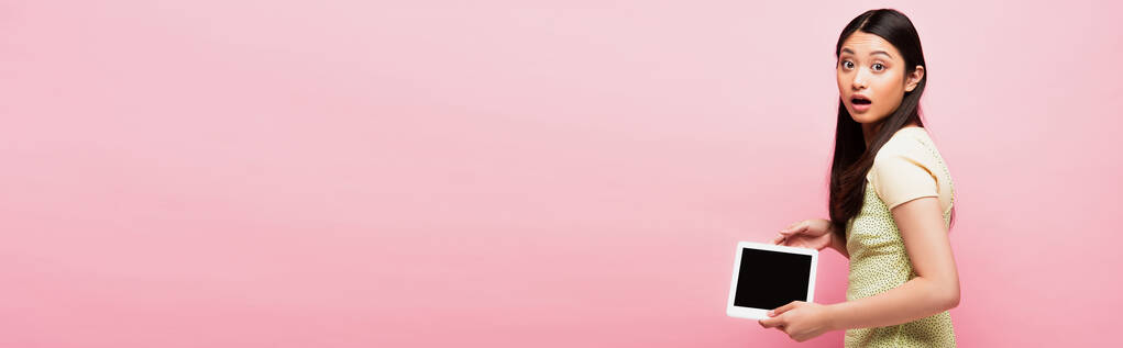 горизонтальне зображення здивованої азіатки, що тримає цифровий планшет з порожнім екраном ізольовано на рожевому
  - Фото, зображення