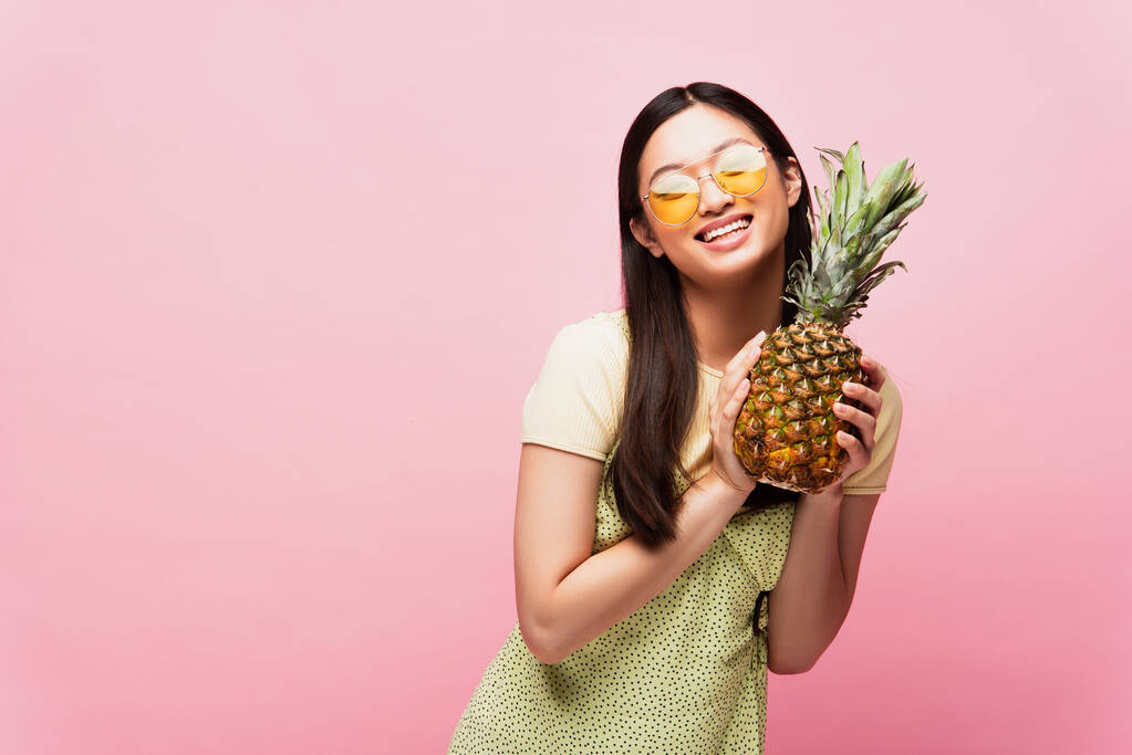 Güneş gözlüklü mutlu Asyalı kız pembe üzerinde taze ananas tutuyor.  - Fotoğraf, Görsel