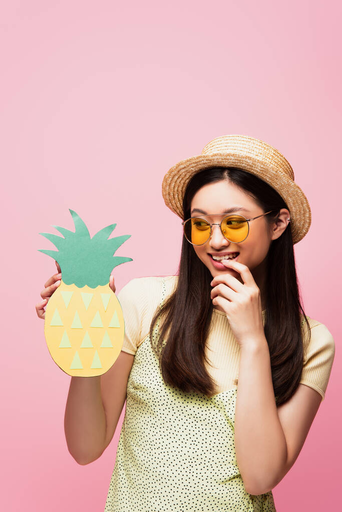 幸せなアジアの女の子でサングラスと藁帽子紙のパイナップルを見てピンクの上に隔離 ロイヤリティフリー写真 画像素材