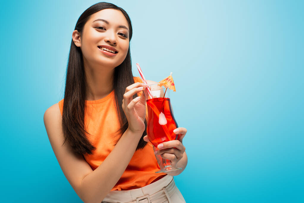 felice ragazza asiatica in possesso di vetro con cocktail su blu - Foto, immagini
