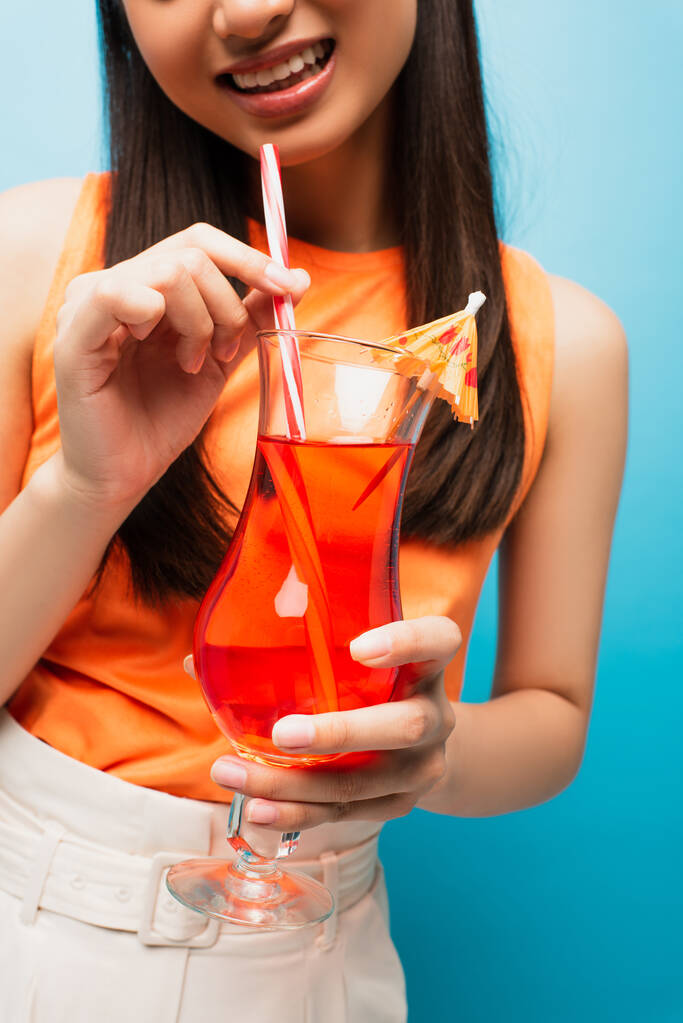 vue recadrée de gaie fille tenant verre avec cocktail sur bleu - Photo, image