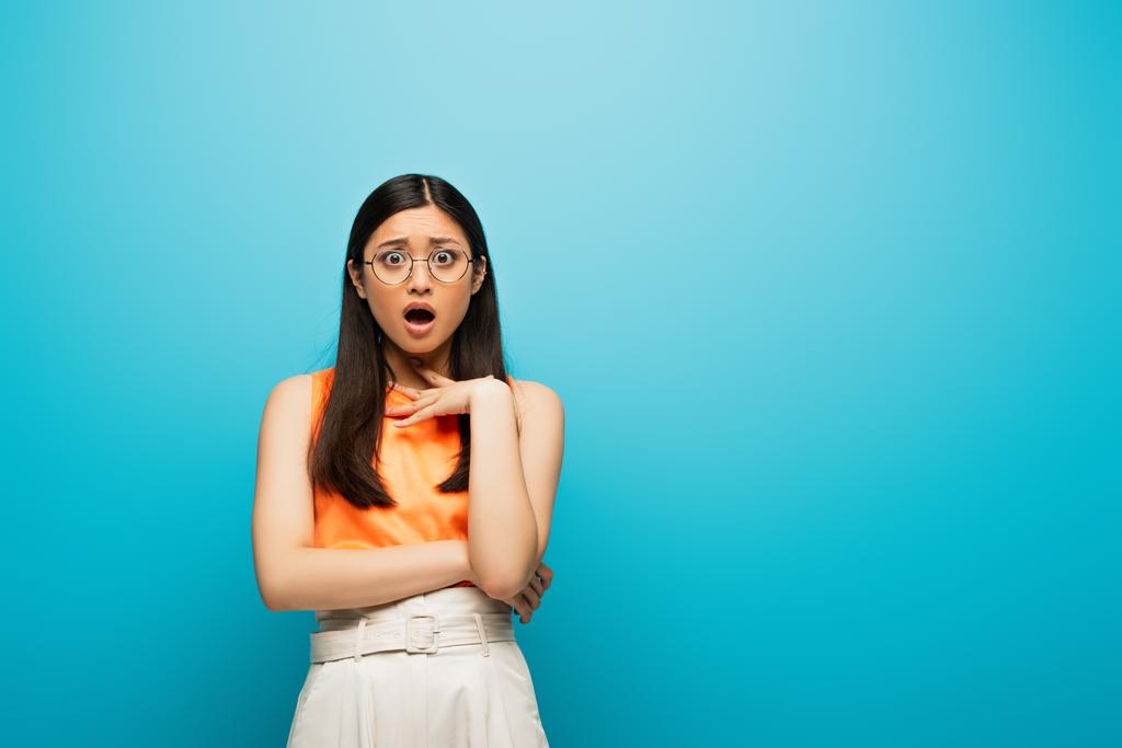 здивована азіатська жінка в окулярах стоїть на синьому
 - Фото, зображення