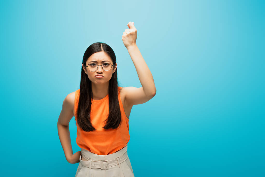 frustrado asiático chica en gafas mostrando apretado puño en azul - Foto, Imagen