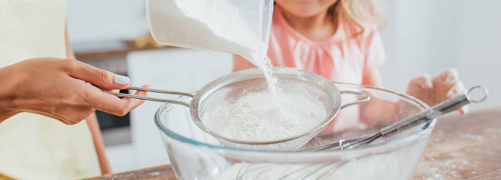częściowy widok kobiety przesiewania mąki do szklanej miski w pobliżu córki, obraz poziomy   - Zdjęcie, obraz