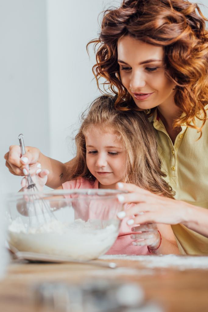 selective focus of young mother kneading dough in glass bowl near daughter - Photo, Image