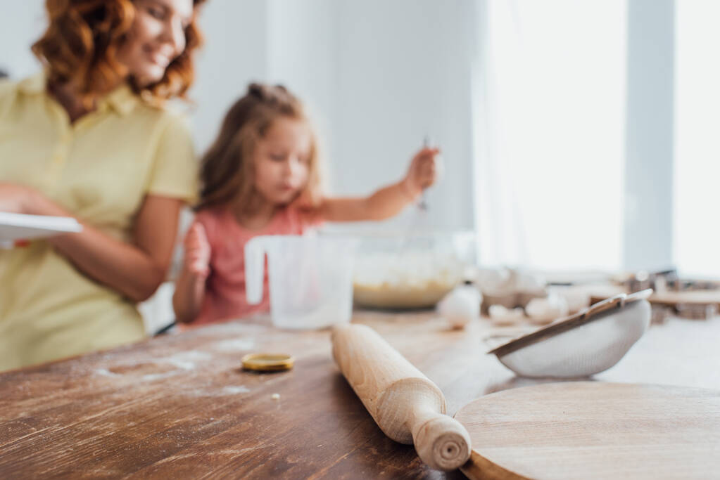 valikoiva painopiste leikkuulauta, valssaustappi ja seula lähellä äiti ja tytär ruoanlaitto keittiössä - Valokuva, kuva