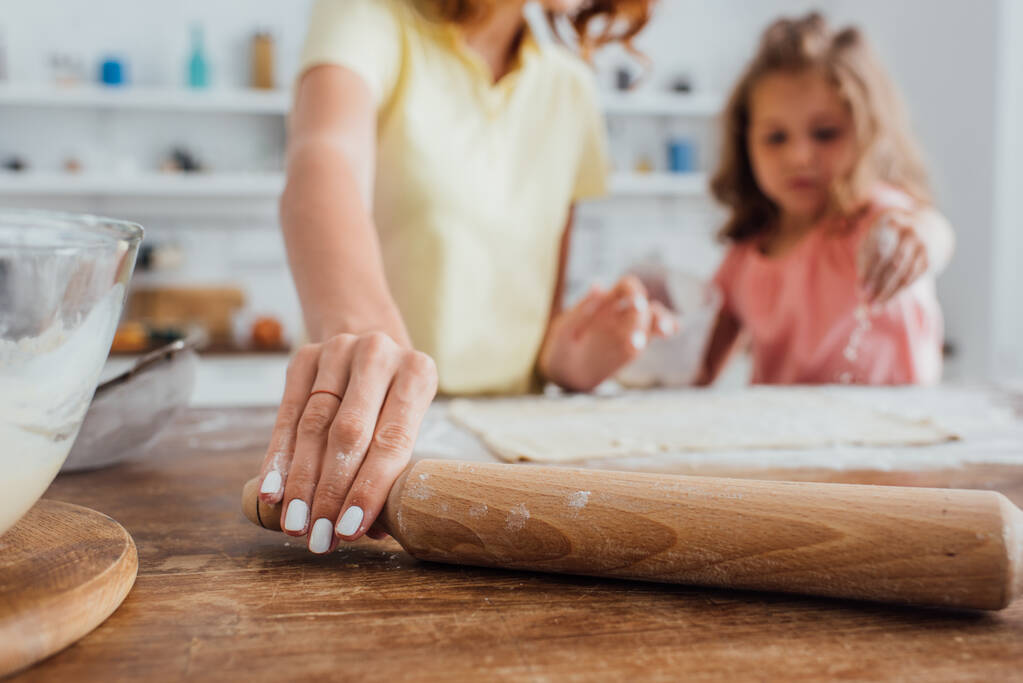 обрезанный вид матери принимая скалку рядом с дочерью и тесто на кухонном столе, избирательный фокус  - Фото, изображение