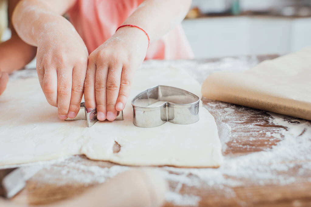 cropped view of child cutting out cookings from rolled dough on table scattered with flour - Photo, Image