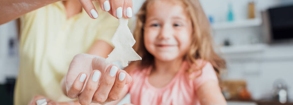 visão parcial da mulher segurando biscoito cru em forma de árvore perto da filha e papel manteiga, imagem horizontal
 - Foto, Imagem