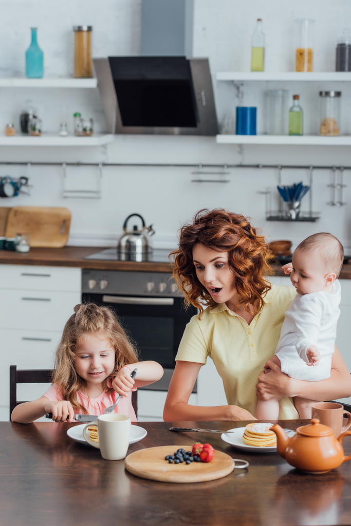 Mutter überrascht mit kleinem Sohn in der Nähe ihrer Tochter beim Frühstück mit Pfannkuchen - Foto, Bild