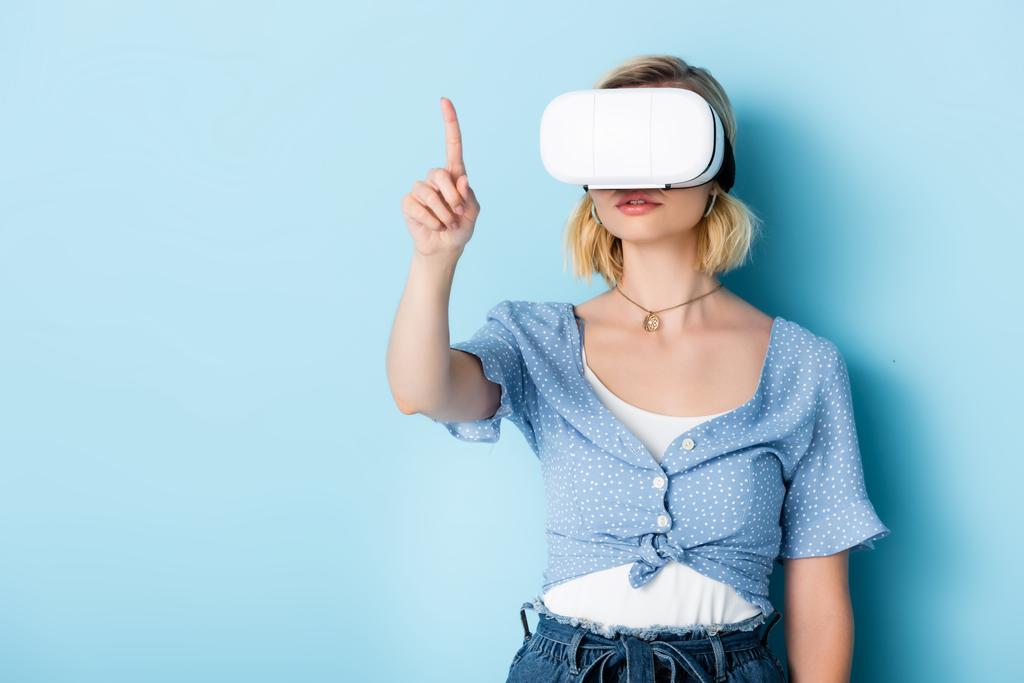 young woman in virtual reality headset pointing with finger on blue  - Photo, Image