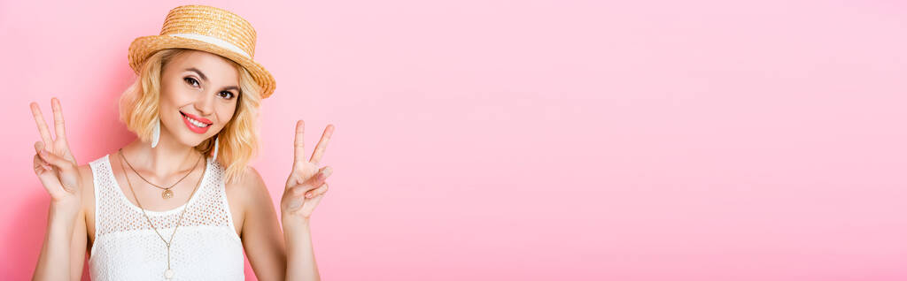 cosecha panorámica de la mujer en sombrero de paja que muestra signo de paz en rosa  - Foto, imagen