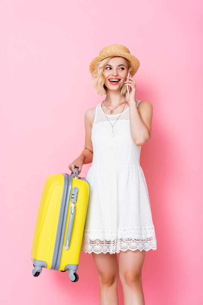 donna in cappello di paglia che tiene i bagagli e parla su smartphone su rosa  - Foto, immagini