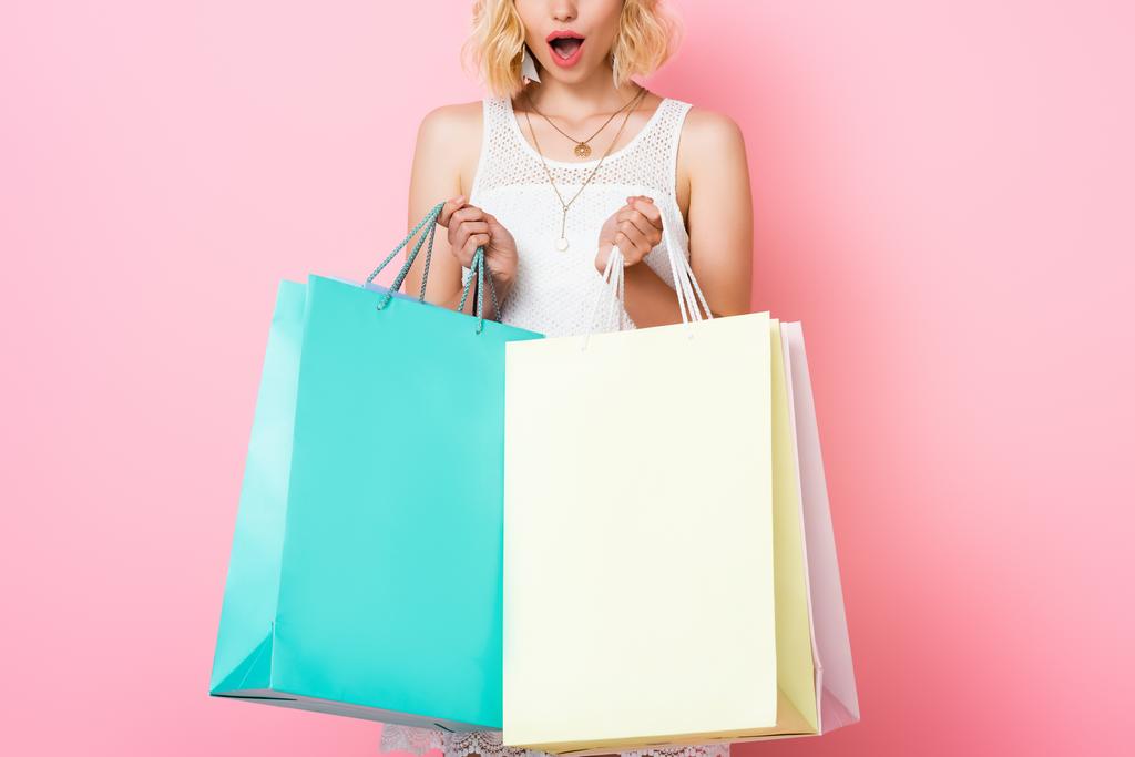 vista ritagliata di donna sorpresa in abito bianco che tiene borse della spesa su rosa  - Foto, immagini