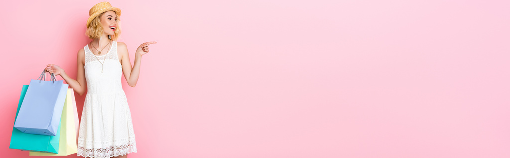ストローハットの女性が指で指してピンクのショッピングバッグを持っているというパノラマの概念  - 写真・画像