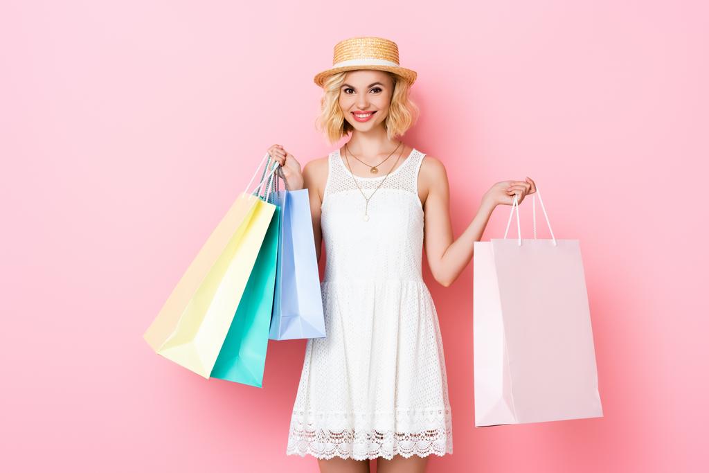 νεαρή γυναίκα σε λευκό φόρεμα κρατώντας τσάντες για ψώνια σε ροζ  - Φωτογραφία, εικόνα