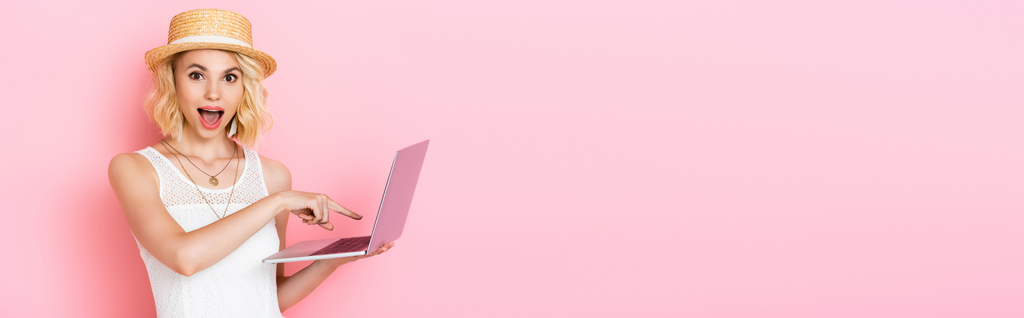 horizontale Ernte von aufgeregten Frau mit Strohhut zeigt mit dem Finger auf Laptop auf rosa - Foto, Bild