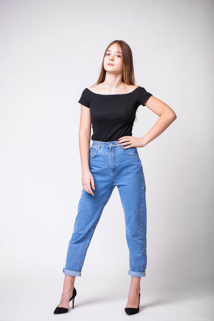 Krásná sexy brunetka v modrých džínách. Módní model v džínových šatech. Izolováno na šedém pozadí studia - Fotografie, Obrázek