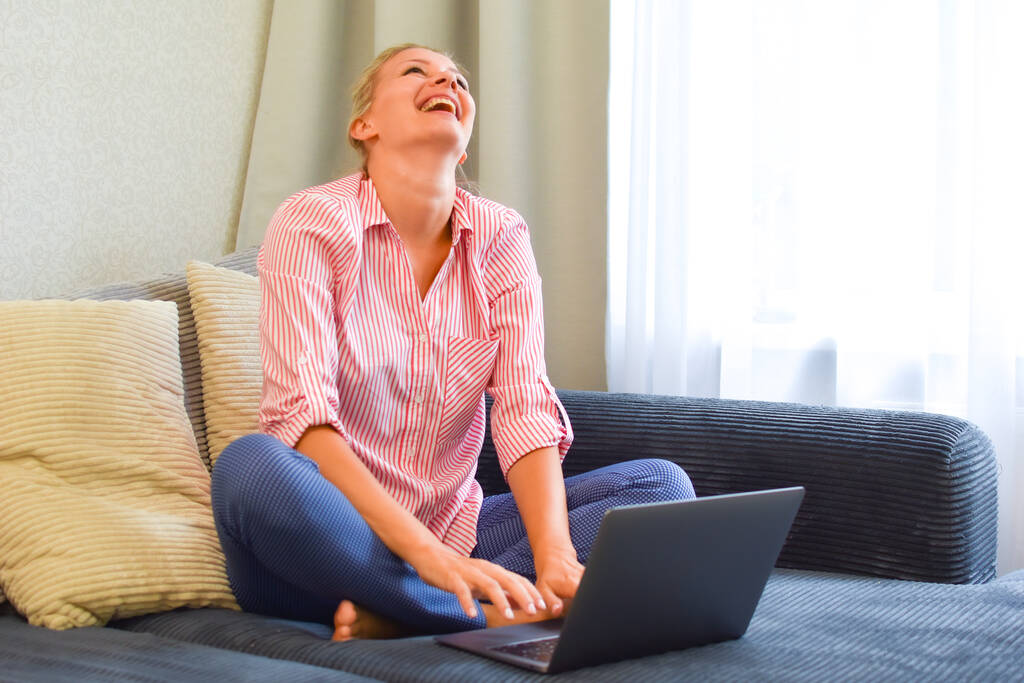 jovem mulher feliz com laptop rindo no sofá em casa
 - Foto, Imagem