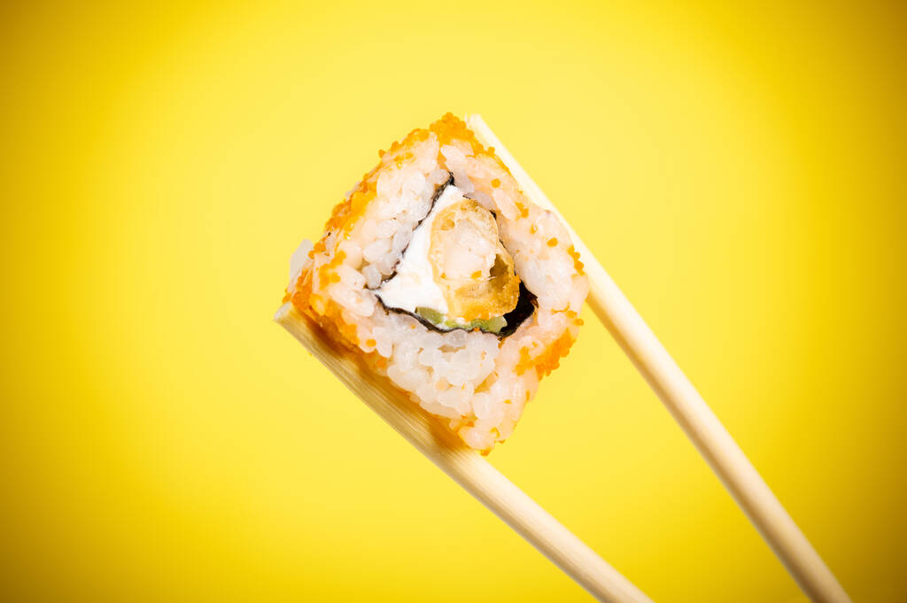 Sushi rotola primo piano in bastoncini di legno su uno sfondo sfumato giallo brillante - Foto, immagini