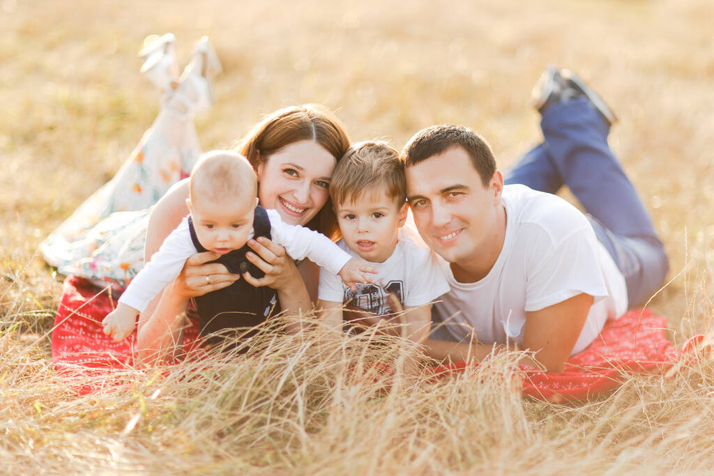 Семья с детьми, гуляющими на открытом воздухе в летнем поле на закате. Отец, мать и двое сыновей веселятся в летнем поле. Человек, семейный день и образ жизни - Фото, изображение