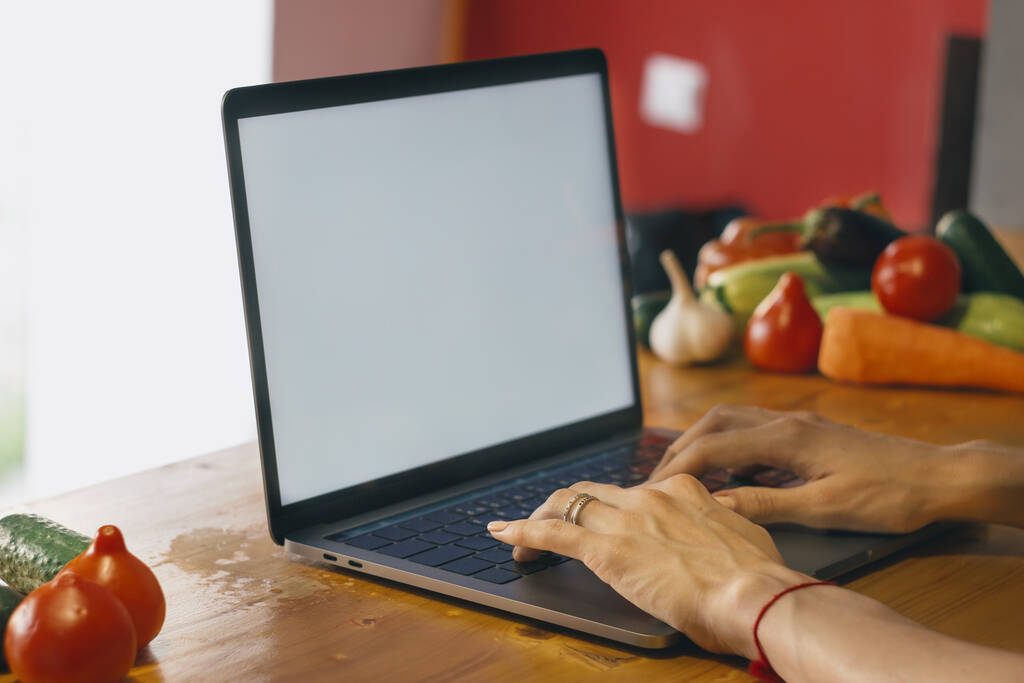 Белый экран. Молодая девушка на кухне с ноутбуком ищет рецепт. Концепция пищевого блогера.  - Фото, изображение