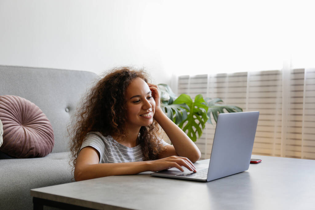 Egy fiatal nő portréja sötét bőrrel és hosszú göndör hajjal a laptopján. Afrikai amerikai nő videóhívással. Szabadúszó az irodában. Közelkép, másolás tér, háttér. - Fotó, kép