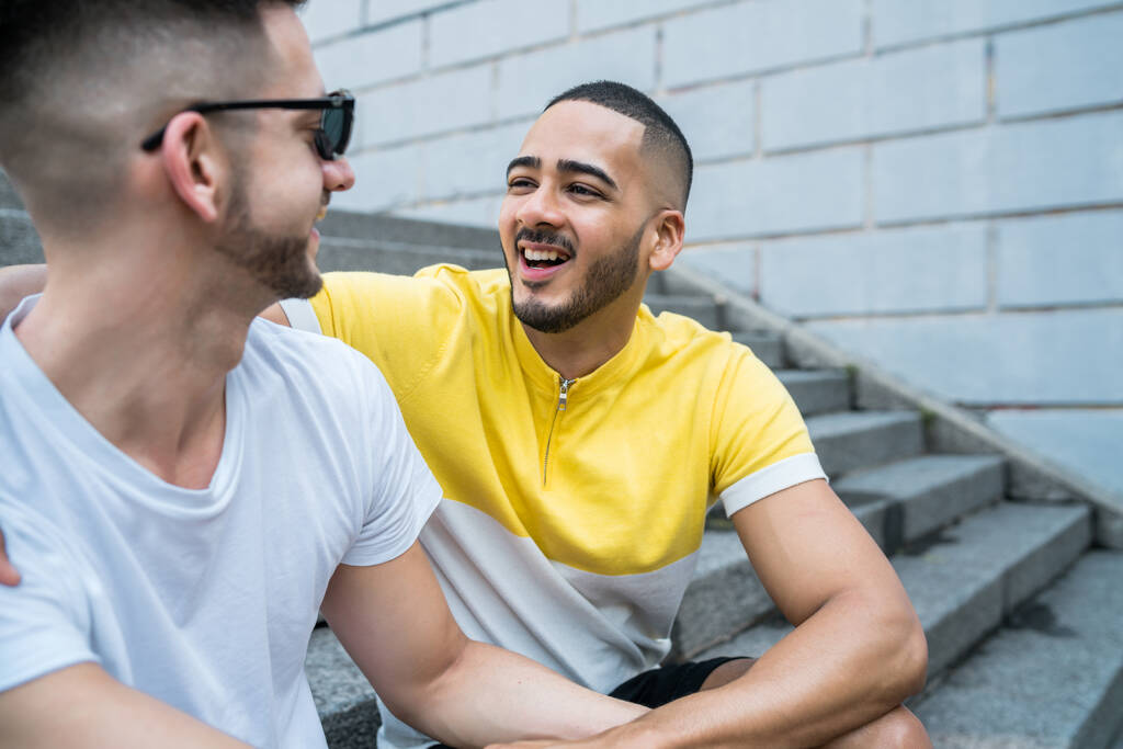 Portrait of happy gay couple spending time together while sitting on stairs outdoors. Lgbt and love concept. - Photo, Image