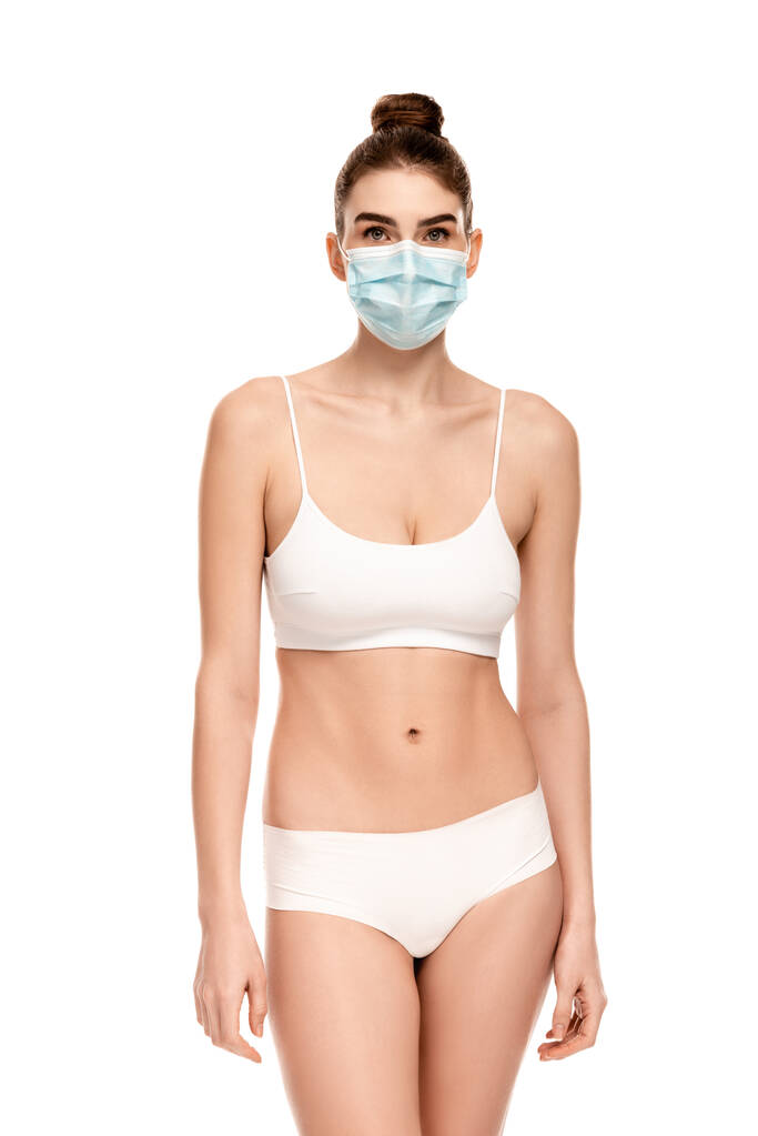 νεαρή γυναίκα με ιατρική μάσκα, πάνω μέρος και κιλότα που απομονώνονται σε λευκό - Φωτογραφία, εικόνα
