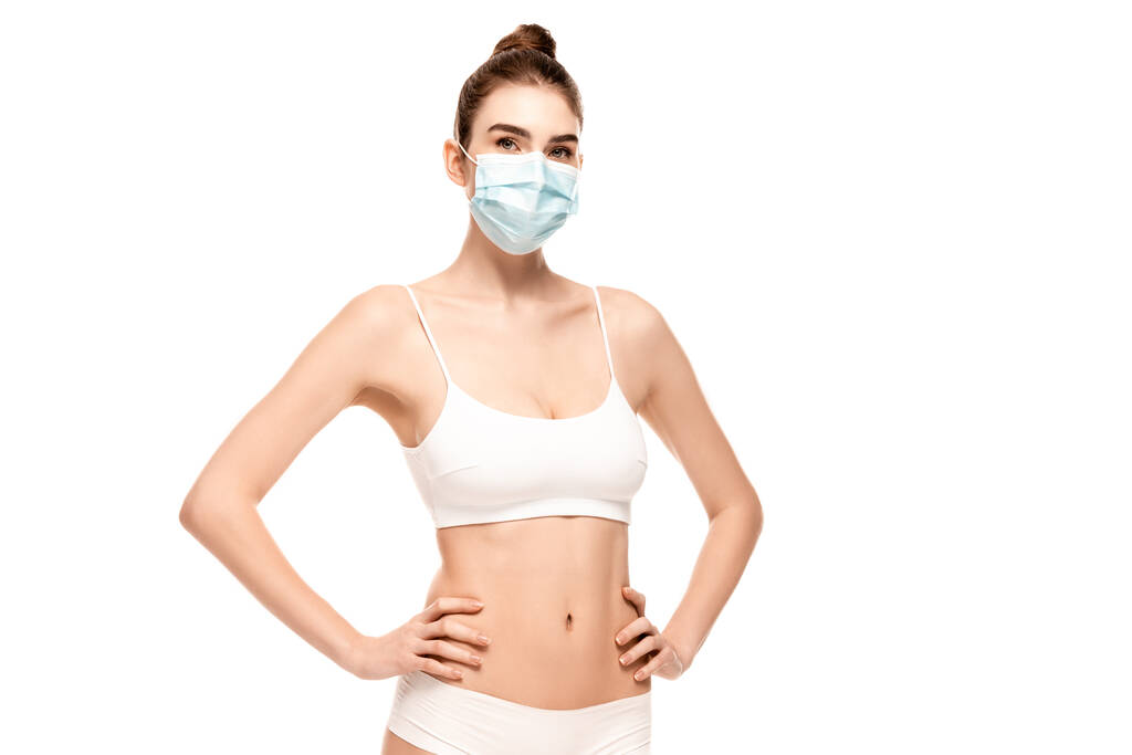 молода жінка в медичній масці, зверху і трусики, що стоять руками на стегнах ізольовані на білому
 - Фото, зображення