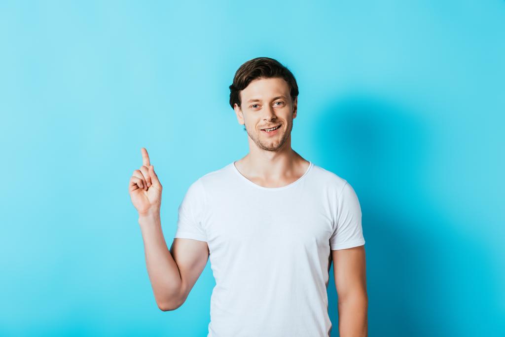 Mężczyzna w białym t-shirt wskazując palcem na niebieskim tle - Zdjęcie, obraz