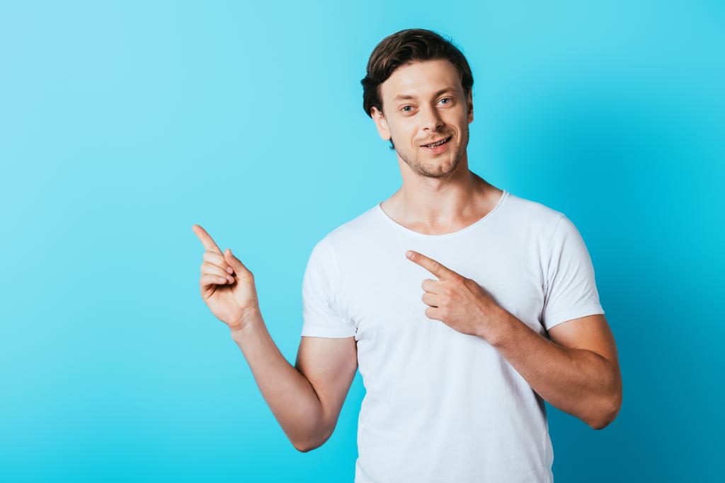 Мужчина в белой футболке показывает пальцами на голубом фоне - Фото, изображение