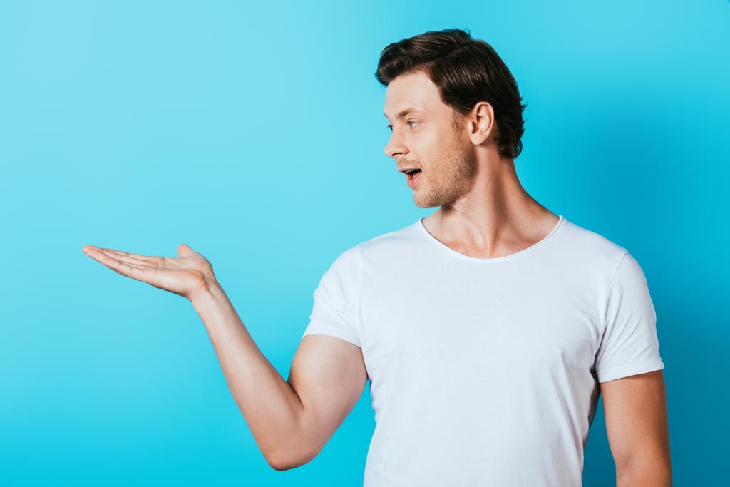 Άνδρας με λευκό t-shirt που δείχνει με το χέρι σε μπλε φόντο - Φωτογραφία, εικόνα