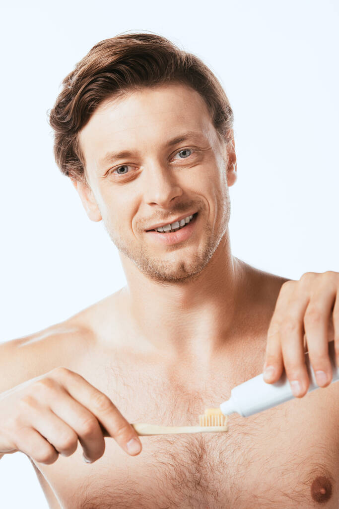 Valikoiva painopiste paidaton mies katselee kameraa pitäen hammastahnaa ja hammasharjaa eristetty valkoinen - Valokuva, kuva