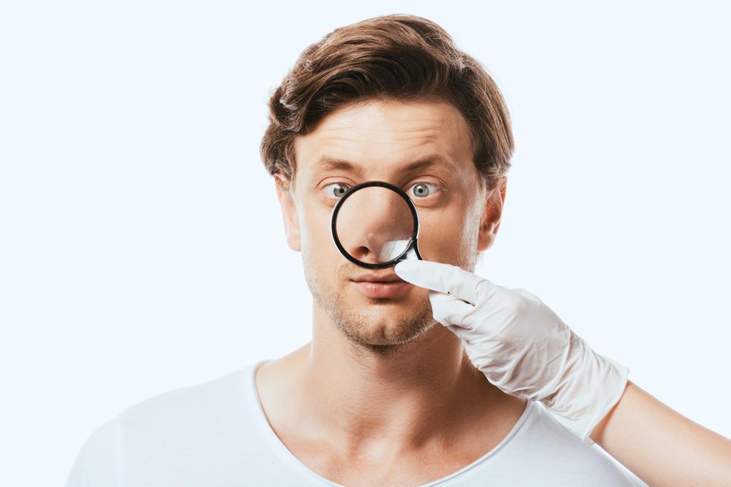 Dermatólogo en guante de látex sosteniendo lupa cerca de la nariz del paciente aislado en blanco - Foto, imagen