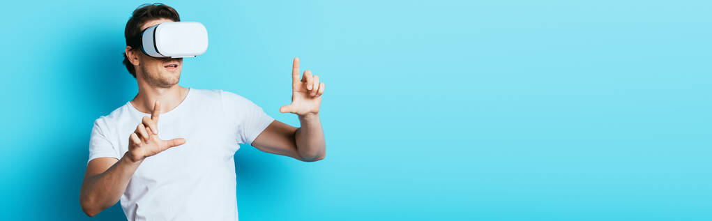 Horizontal crop of man in vr headset pointing with fingers on blue background - Photo, Image