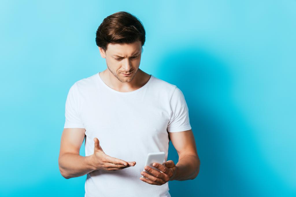 Νεαρός που δείχνει με το χέρι ενώ χρησιμοποιεί smartphone σε μπλε φόντο - Φωτογραφία, εικόνα