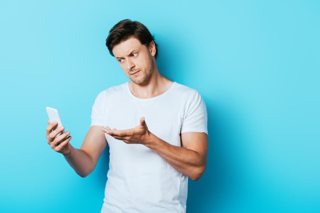 Ernsthafter Mann zeigt mit der Hand auf Smartphone auf blauem Hintergrund - Foto, Bild