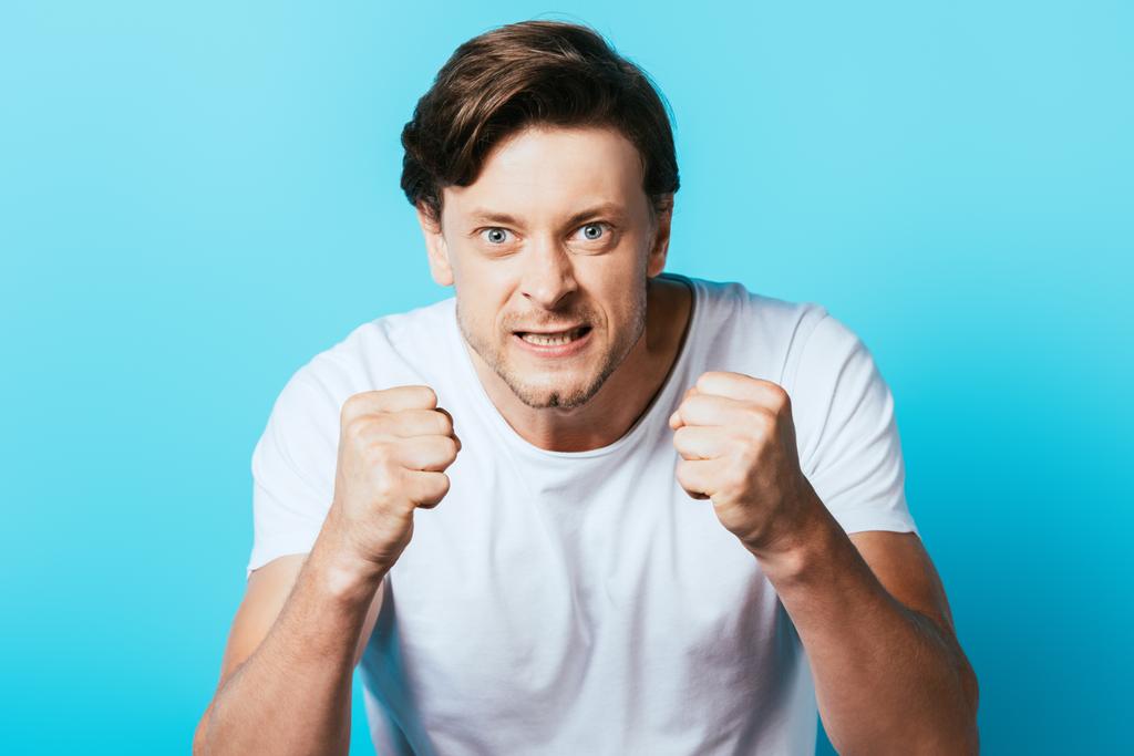 Aggressiver Mann im weißen T-Shirt mit Fäusten auf blauem Hintergrund - Foto, Bild