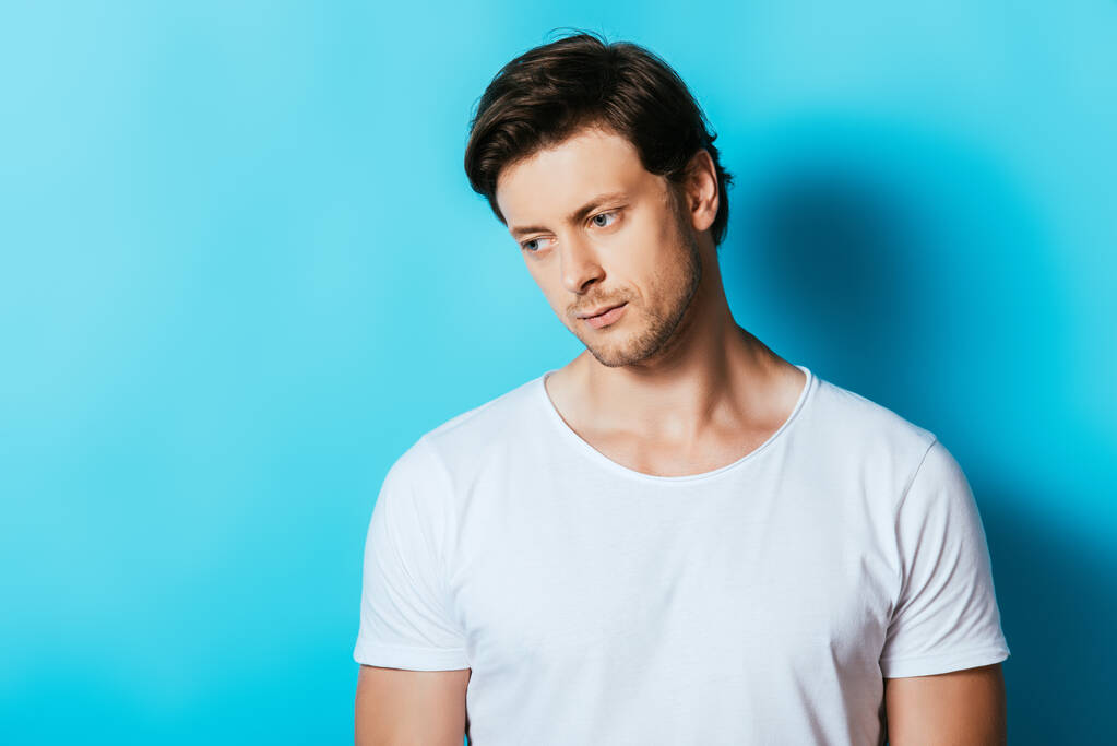 Upset man in white t-shirt looking away on blue background - Photo, Image