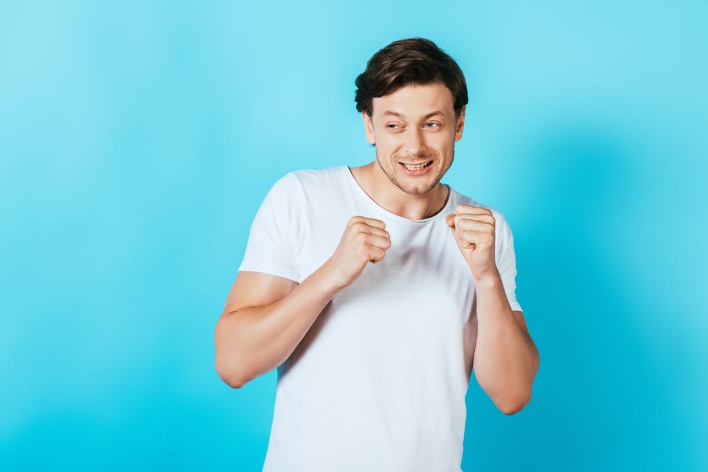 Scared man with hands in fists looking away on blue background - Photo, Image