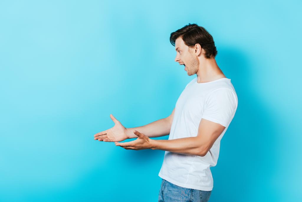 Wstrząśnięty mężczyzna wskazujący dłońmi na niebieskim tle - Zdjęcie, obraz