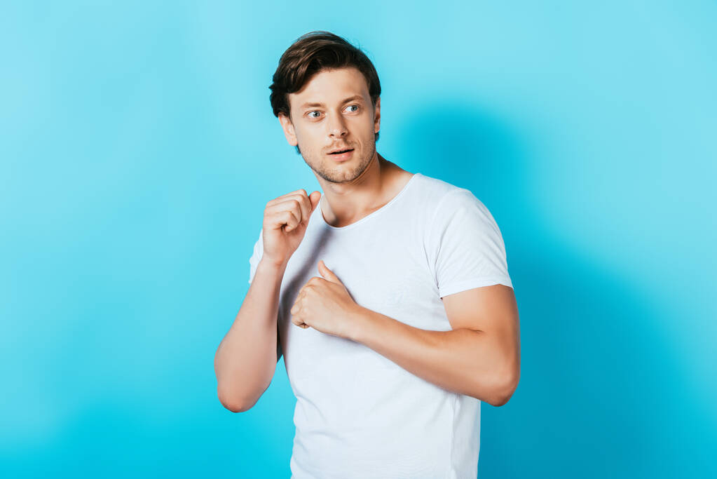 Fiatal férfi fehér pólóban néz félre a kék háttér - Fotó, kép