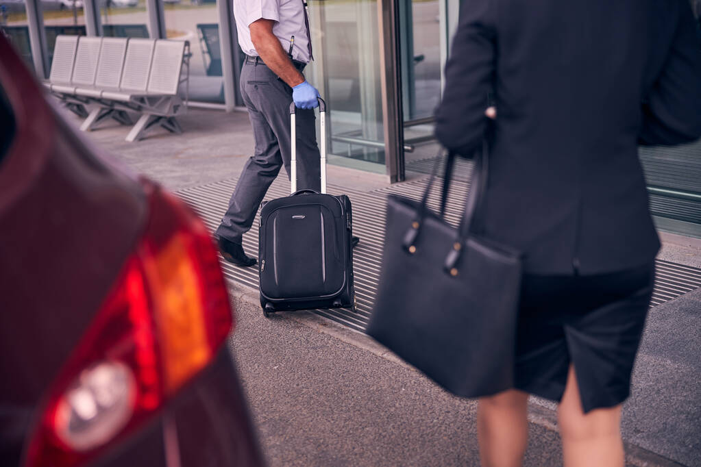 Сотрудник аэропорта мужчина помогает бизнесвумен нести багаж - Фото, изображение