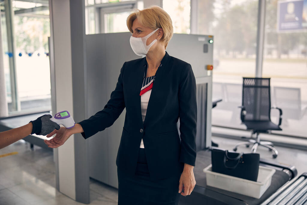 Охоронець аеропорту вимірює температуру пані перед польотом
 - Фото, зображення