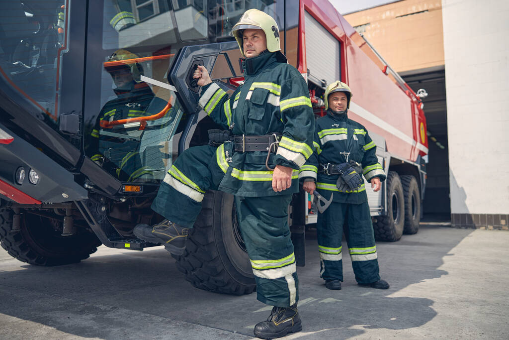 Mann setzt Fuß auf Stufe des großen roten Feuerwehrfahrzeugs - Foto, Bild