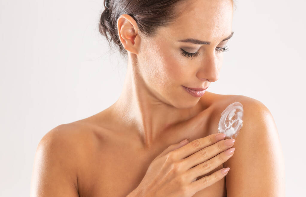 Mulher bonita aplicando creme em seu ombro isolado em branco. Skincare spa conceito de bem-estar e cosméticos
.  - Foto, Imagem